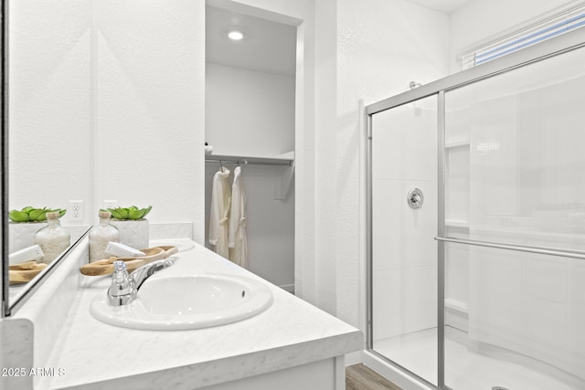 bathroom featuring double vanity, a textured wall, a spacious closet, a shower stall, and a sink