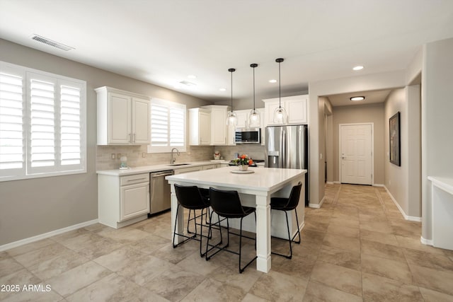 kitchen featuring a kitchen breakfast bar, light countertops, backsplash, visible vents, and stainless steel appliances