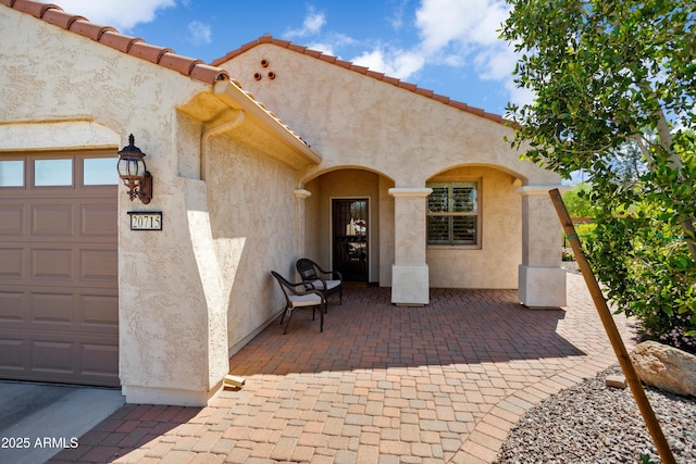 view of exterior entry with stucco siding, a tiled roof, and an attached garage