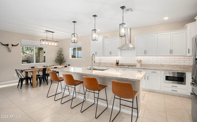 kitchen featuring a center island with sink, appliances with stainless steel finishes, decorative light fixtures, sink, and white cabinets