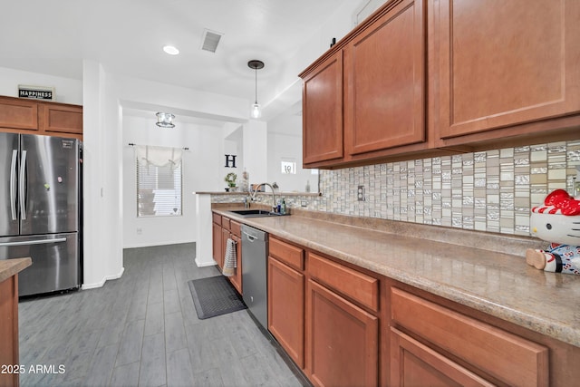 kitchen with appliances with stainless steel finishes, pendant lighting, tasteful backsplash, sink, and light hardwood / wood-style flooring