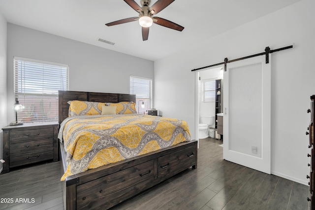 bedroom with a barn door, dark wood-type flooring, ceiling fan, and ensuite bath