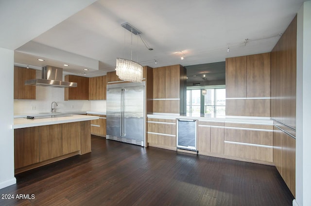 kitchen featuring sink, hanging light fixtures, beverage cooler, wall chimney range hood, and stainless steel built in fridge