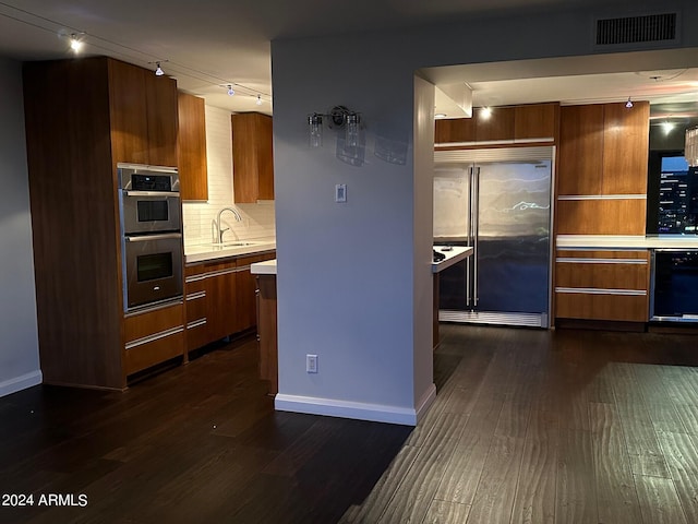 kitchen featuring dark wood-type flooring, track lighting, sink, decorative backsplash, and stainless steel appliances