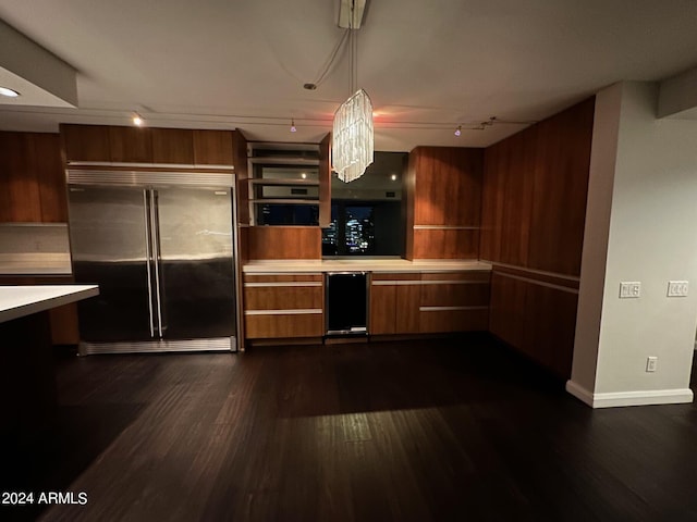 kitchen featuring track lighting, stainless steel built in fridge, hanging light fixtures, and dark wood-type flooring