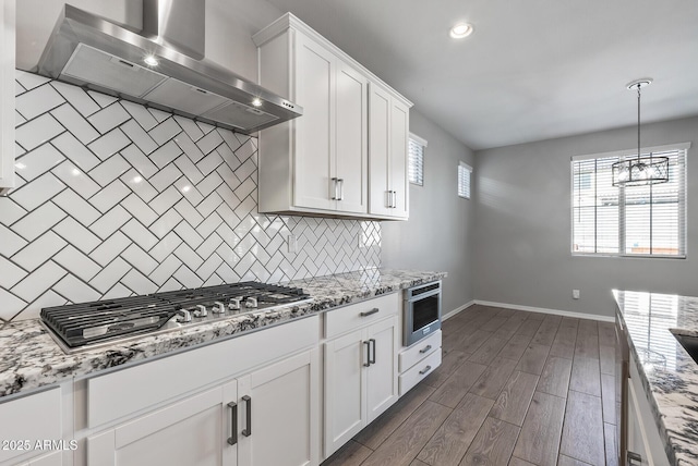 kitchen featuring stainless steel appliances, wall chimney range hood, and white cabinetry