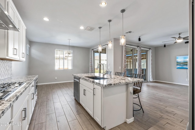 kitchen featuring wall chimney exhaust hood, a kitchen island with sink, white cabinets, ceiling fan, and sink