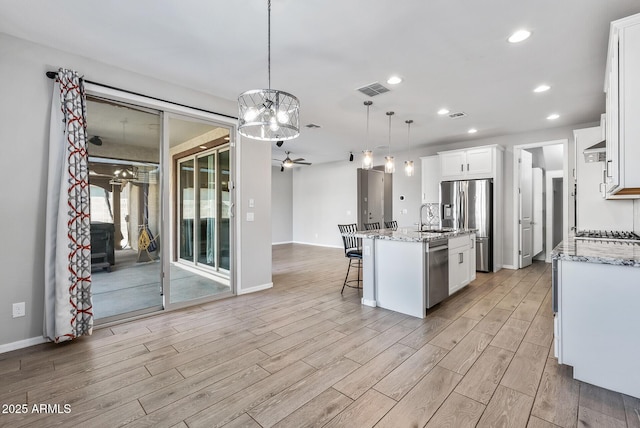 kitchen featuring sink, decorative light fixtures, white cabinetry, ceiling fan with notable chandelier, and a center island with sink