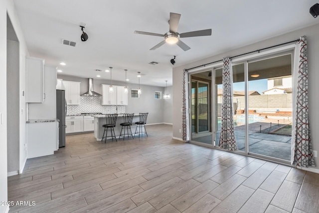 kitchen with wall chimney exhaust hood, a center island, a breakfast bar, stainless steel refrigerator, and white cabinets