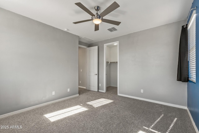 unfurnished bedroom featuring a walk in closet, dark carpet, a closet, and ceiling fan