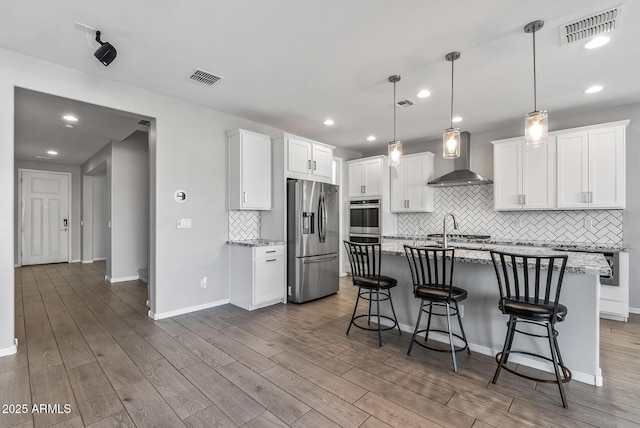 kitchen featuring decorative light fixtures, white cabinets, appliances with stainless steel finishes, and wall chimney exhaust hood