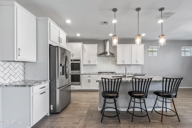 kitchen with wall chimney range hood, white cabinetry, hanging light fixtures, and appliances with stainless steel finishes