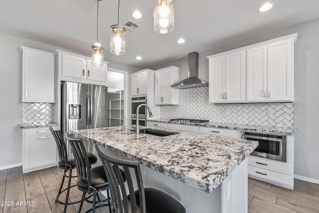 kitchen with decorative light fixtures, white cabinetry, an island with sink, and wall chimney exhaust hood