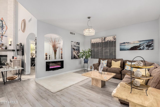 337 E Clairidge Dr, San Tan Valley, AZ 85143 - living room featuring arched walkways, a chandelier, visible vents, light wood finished floors, and a glass covered fireplace