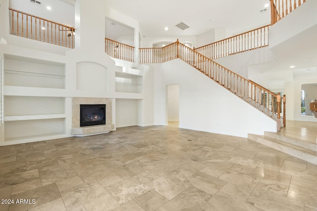 unfurnished living room with built in features, a high ceiling, and a tiled fireplace