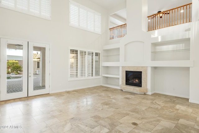 unfurnished living room with a tiled fireplace, built in features, a high ceiling, and french doors