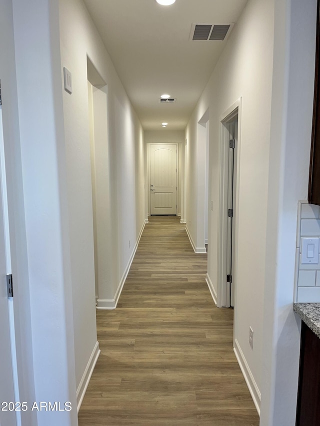 corridor with baseboards, visible vents, and wood finished floors