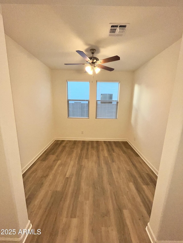 empty room featuring a ceiling fan, baseboards, visible vents, and dark wood finished floors
