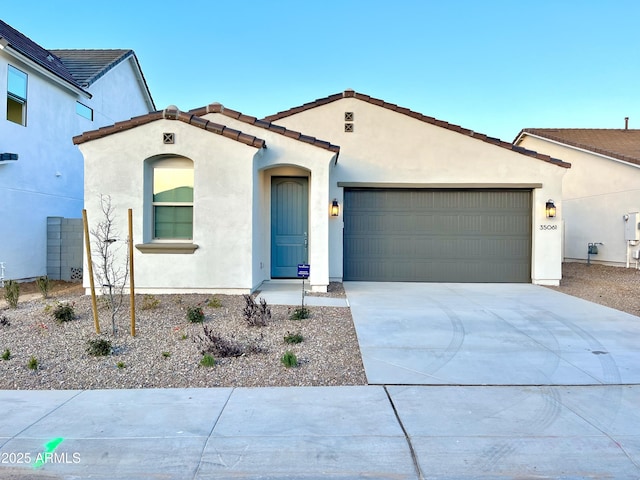 mediterranean / spanish-style home with stucco siding, a tiled roof, driveway, and a garage