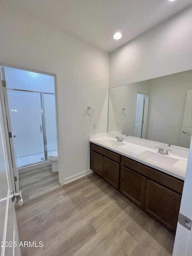 full bathroom featuring a sink, double vanity, toilet, a shower stall, and wood finished floors