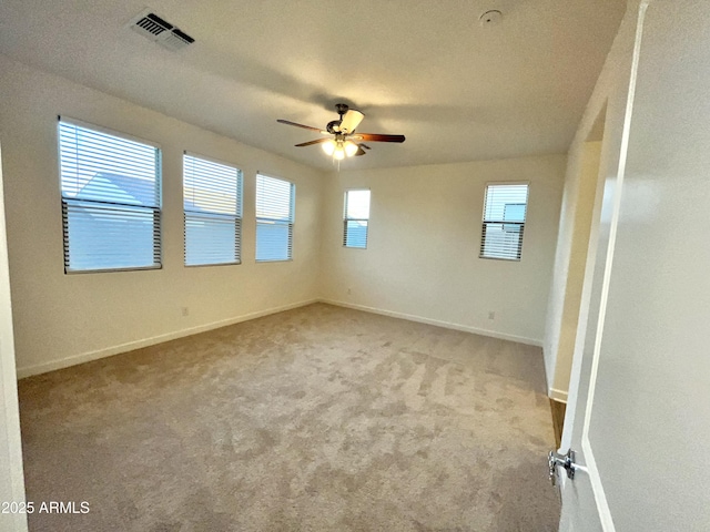 carpeted spare room featuring ceiling fan, visible vents, and baseboards