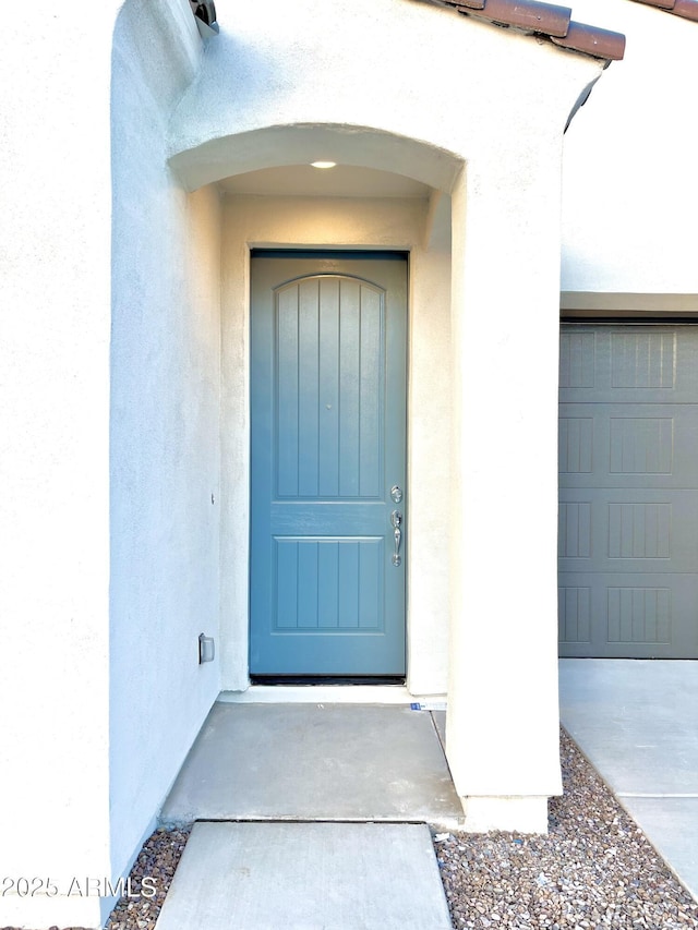 view of exterior entry featuring a garage and stucco siding