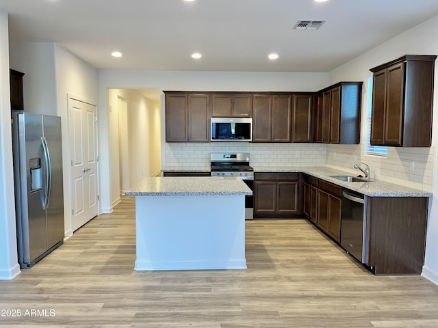 kitchen with dark brown cabinetry, light wood-type flooring, a sink, appliances with stainless steel finishes, and backsplash