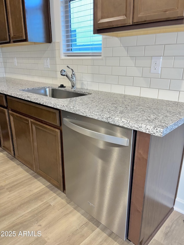 kitchen featuring decorative backsplash, light stone countertops, light wood-type flooring, a sink, and dishwasher