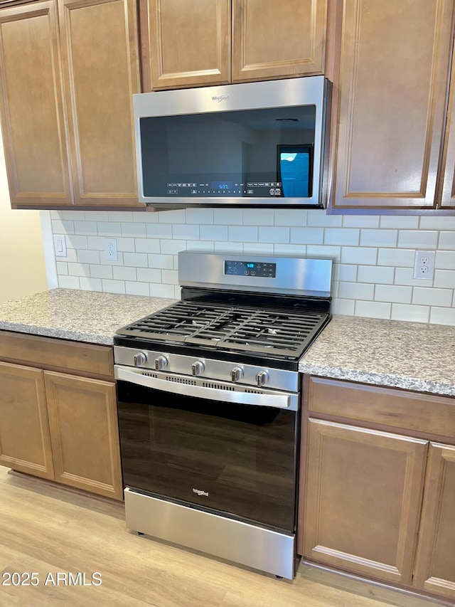 kitchen featuring stainless steel appliances, light stone countertops, light wood finished floors, and tasteful backsplash