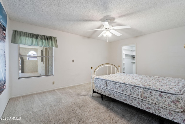 carpeted bedroom with a spacious closet, a textured ceiling, ceiling fan, and a closet