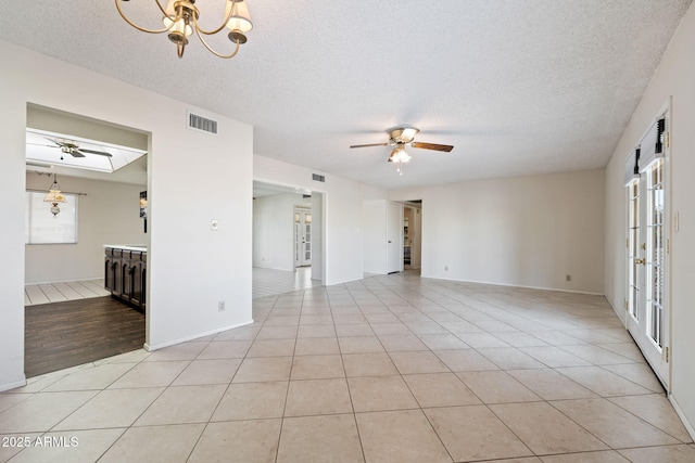 tiled empty room featuring ceiling fan with notable chandelier and a textured ceiling