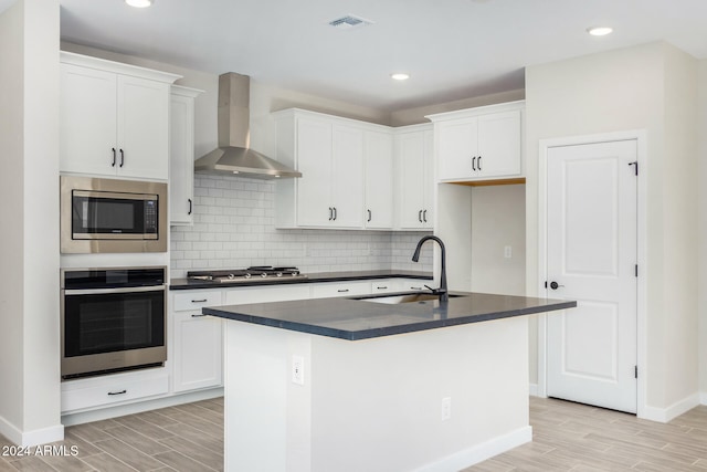 kitchen featuring white cabinetry, wall chimney range hood, a kitchen island with sink, and appliances with stainless steel finishes