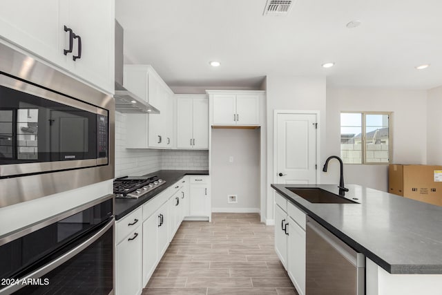 kitchen featuring white cabinetry, sink, wall chimney exhaust hood, a center island with sink, and appliances with stainless steel finishes