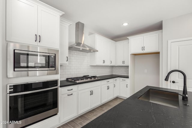 kitchen with white cabinets, appliances with stainless steel finishes, sink, and wall chimney range hood