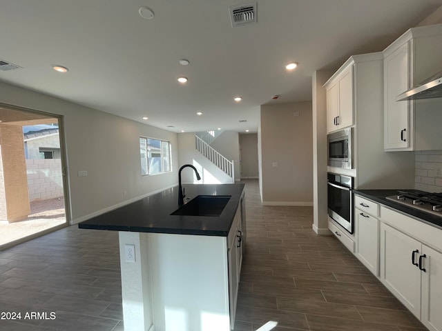 kitchen featuring backsplash, stainless steel appliances, a kitchen island with sink, sink, and white cabinetry