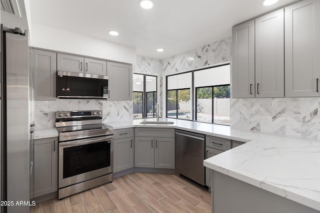 kitchen with appliances with stainless steel finishes, light stone countertops, sink, and gray cabinetry