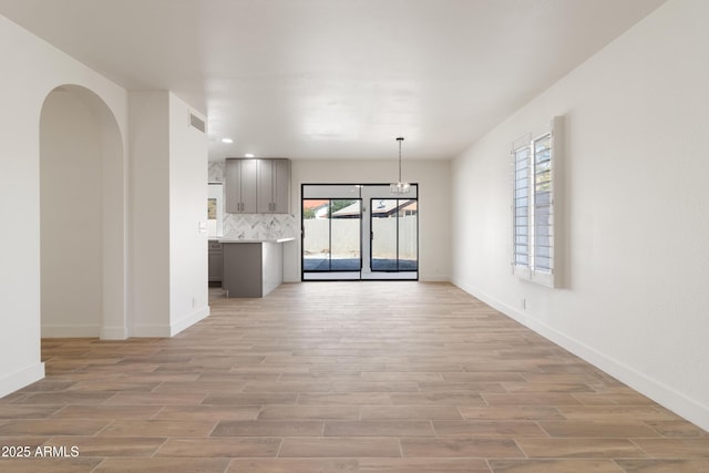 unfurnished living room featuring an inviting chandelier and light hardwood / wood-style flooring