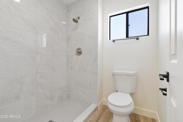 bathroom featuring wood-type flooring, toilet, and a tile shower