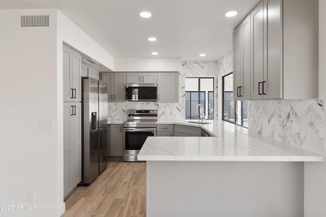 kitchen featuring stainless steel appliances, kitchen peninsula, light stone countertops, and gray cabinetry