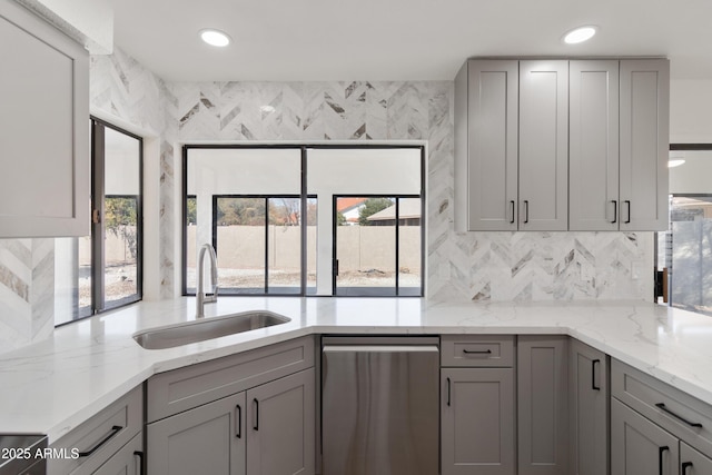 kitchen with gray cabinets, a healthy amount of sunlight, light stone countertops, and sink