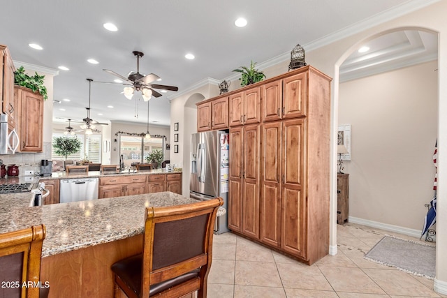 kitchen with light stone counters, arched walkways, stainless steel appliances, ornamental molding, and a peninsula