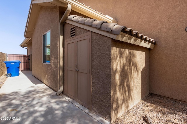 view of side of home with a tile roof, fence, and stucco siding