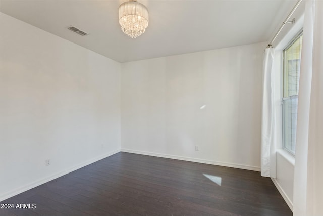 unfurnished room with a notable chandelier and dark hardwood / wood-style floors