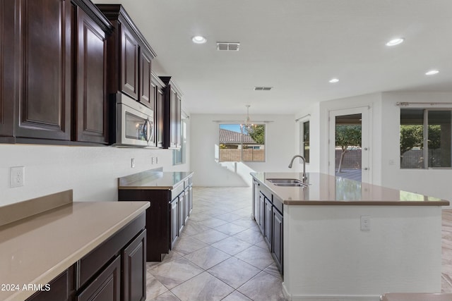 kitchen with dark brown cabinetry, sink, a center island with sink, a notable chandelier, and hanging light fixtures