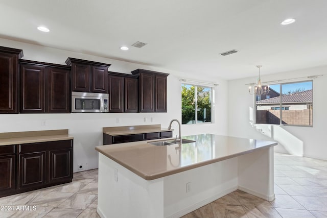 kitchen with pendant lighting, an inviting chandelier, a center island with sink, sink, and dark brown cabinets