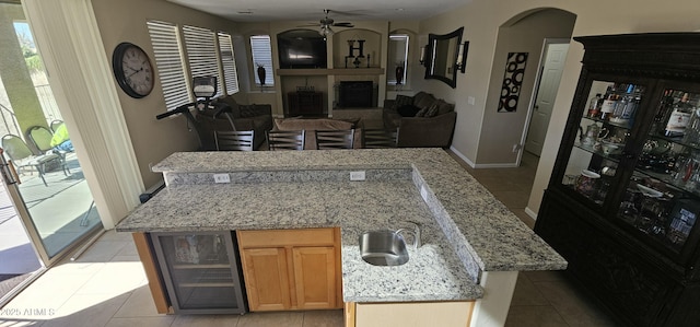 kitchen with sink, beverage cooler, a center island, ceiling fan, and light stone countertops