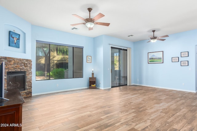 unfurnished living room with ceiling fan, a healthy amount of sunlight, a stone fireplace, and light hardwood / wood-style flooring