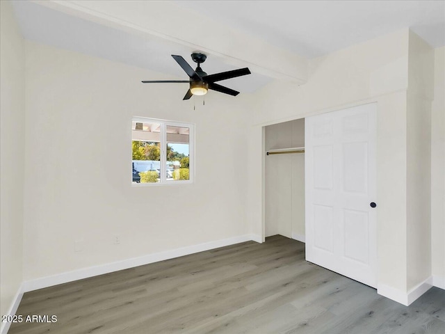 unfurnished bedroom with a closet, wood finished floors, beam ceiling, and baseboards