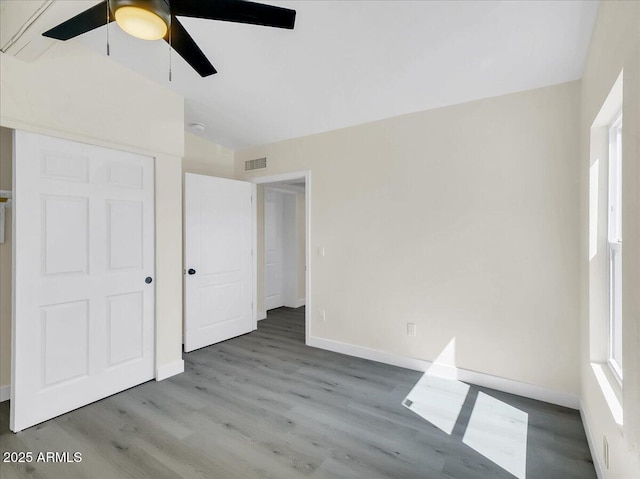 unfurnished bedroom with lofted ceiling, visible vents, baseboards, and wood finished floors