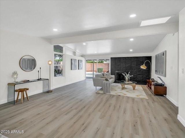 living area featuring vaulted ceiling with beams, light wood-style flooring, a fireplace, and baseboards